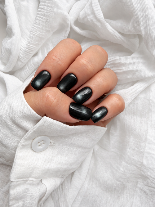 Black Cat Eye press-on nails seen from above on a curled hand against a white shirt cuff